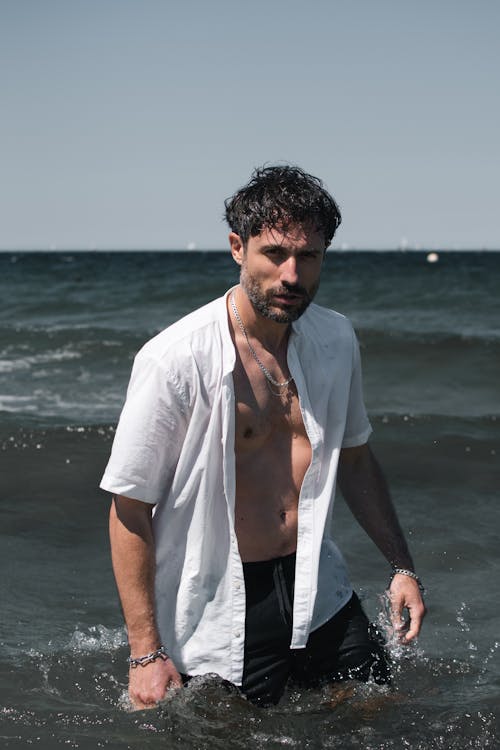 Man in Unzipped Shirt in Sea on Shore