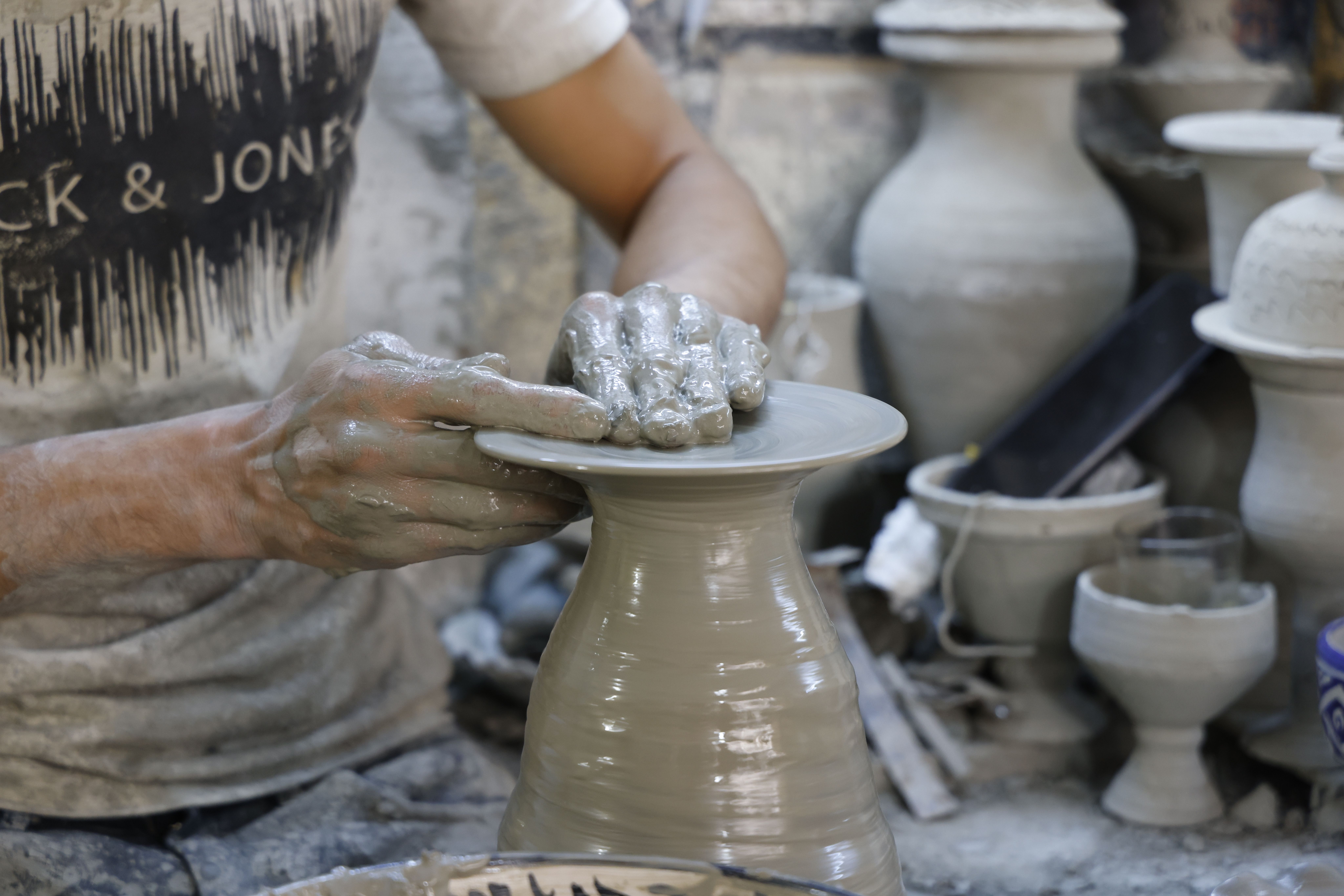 Artisan shaping clay on a pottery wheel, highlighting the craftsmanship and artistry involved.