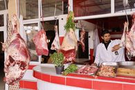 A butcher working at an outdoor market stall with various cuts of beef hanging, showcasing fresh meat preparation.