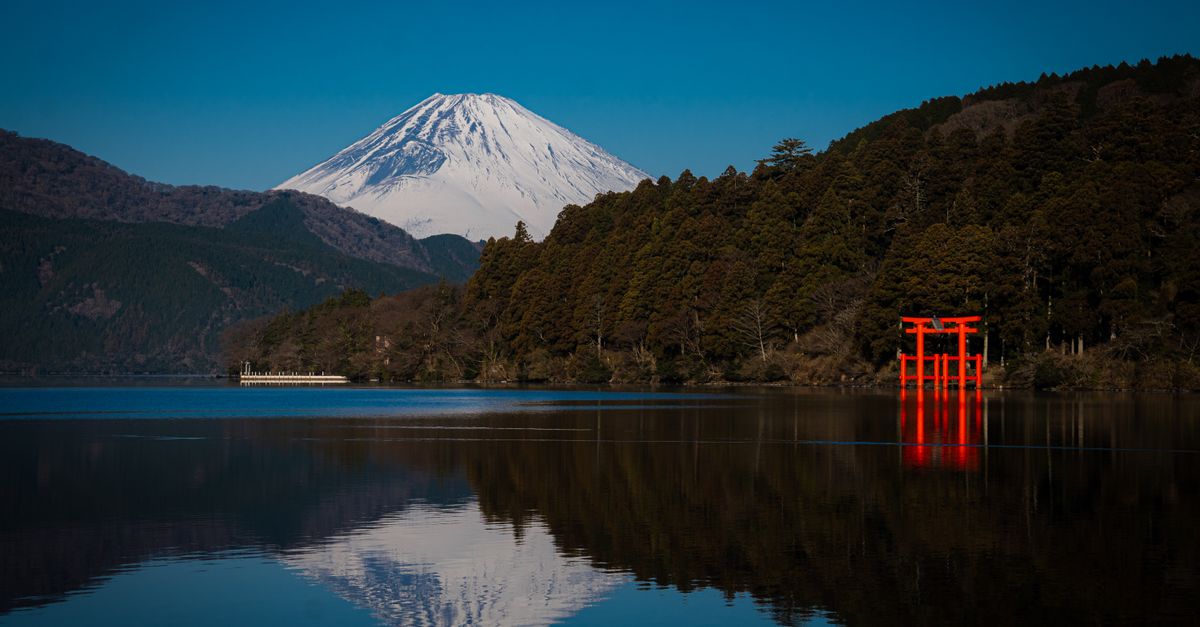 Stunning view of Mount Fuji and a red torii gate reflecting in Lake Ashi, Hakone, Japan.