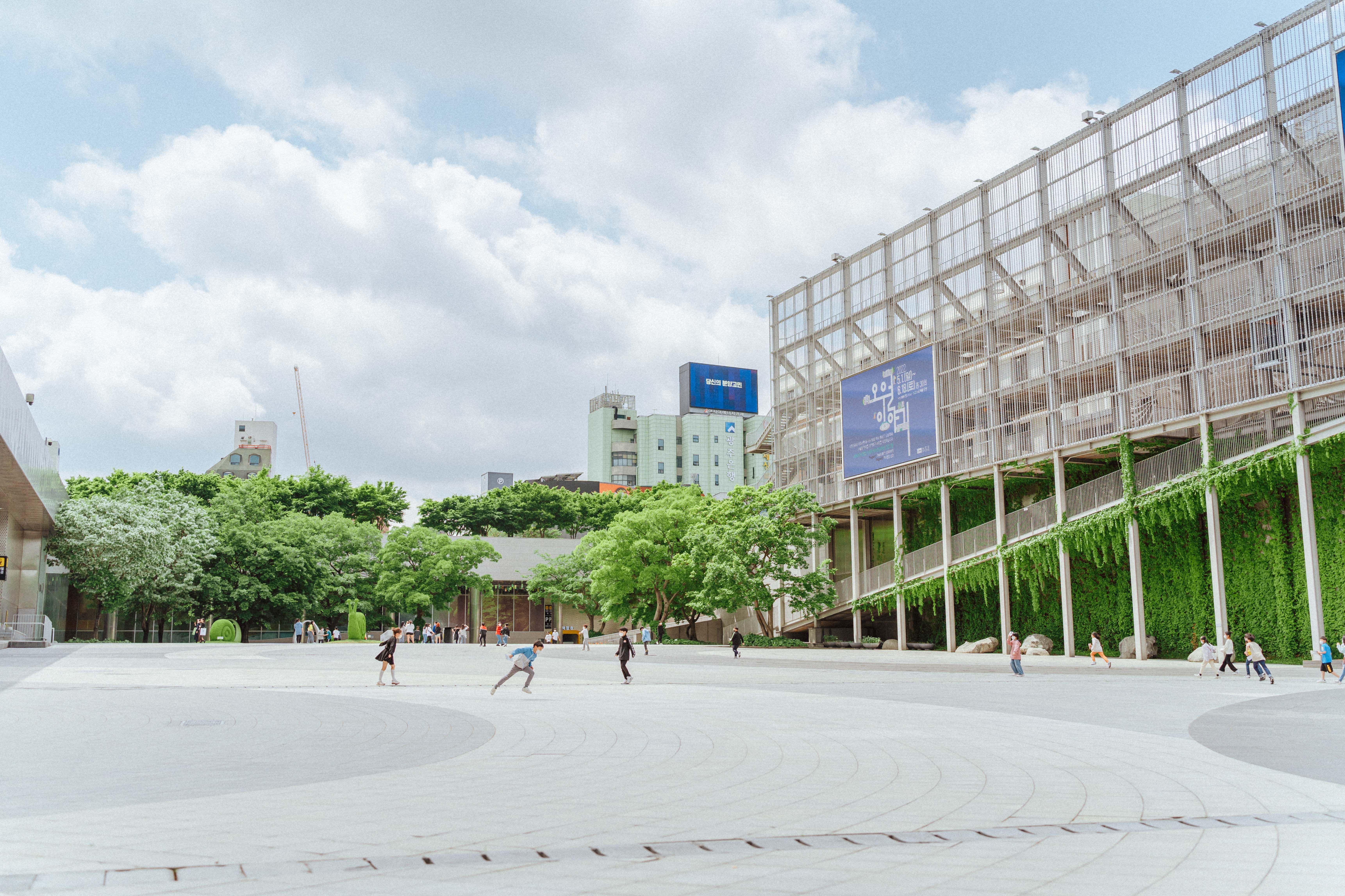 Spacious urban square with modern architecture and greenery, capturing people enjoying the vibrant setting.