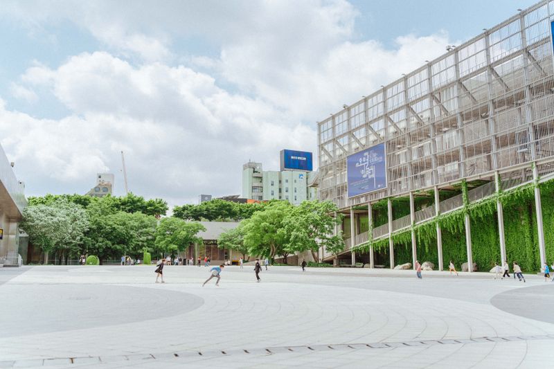 Spacious urban square with modern architecture and greenery, capturing people enjoying the vibrant setting.