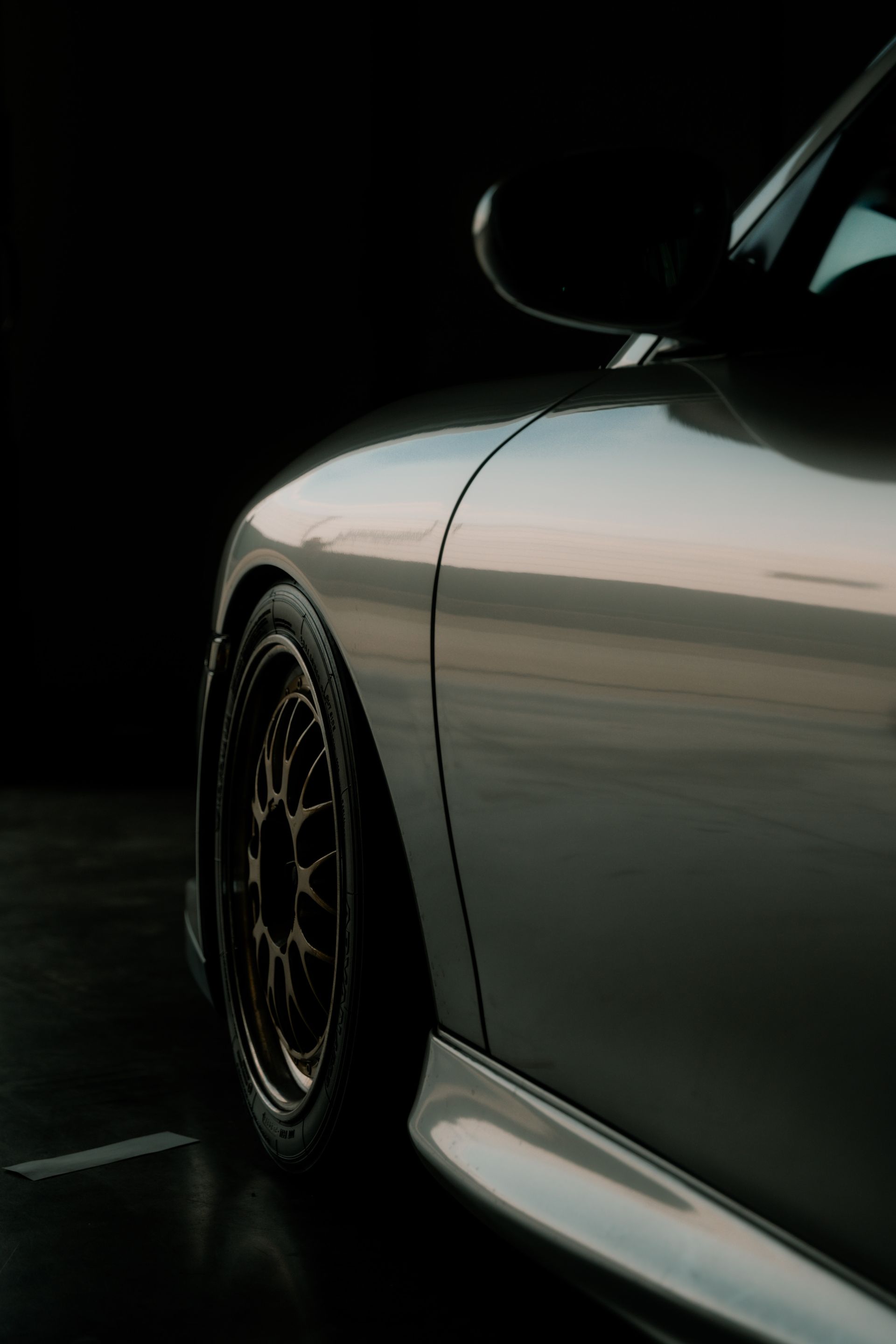 Close-up of a car’s side panel and wheel under moody, low workshop lighting