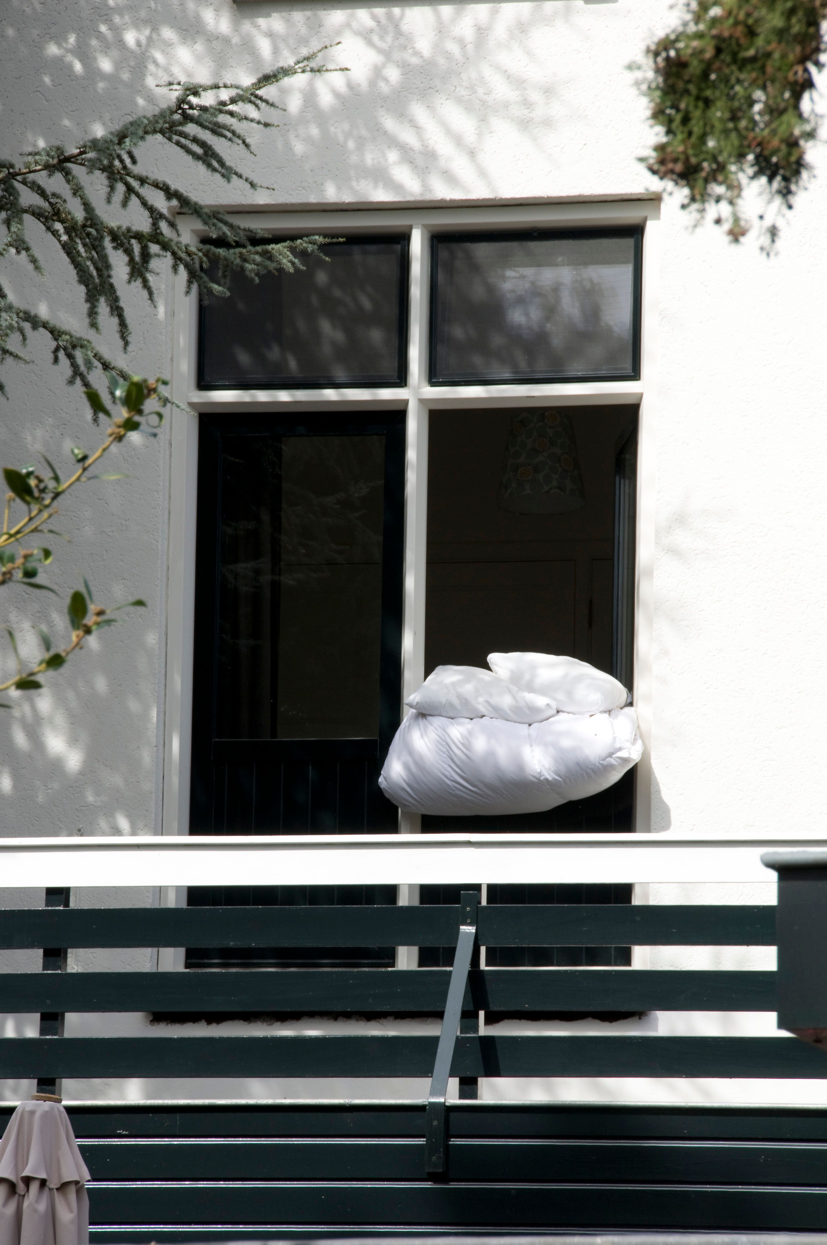 A fresh pillow and duvet airing outside an open window on a sunny day.