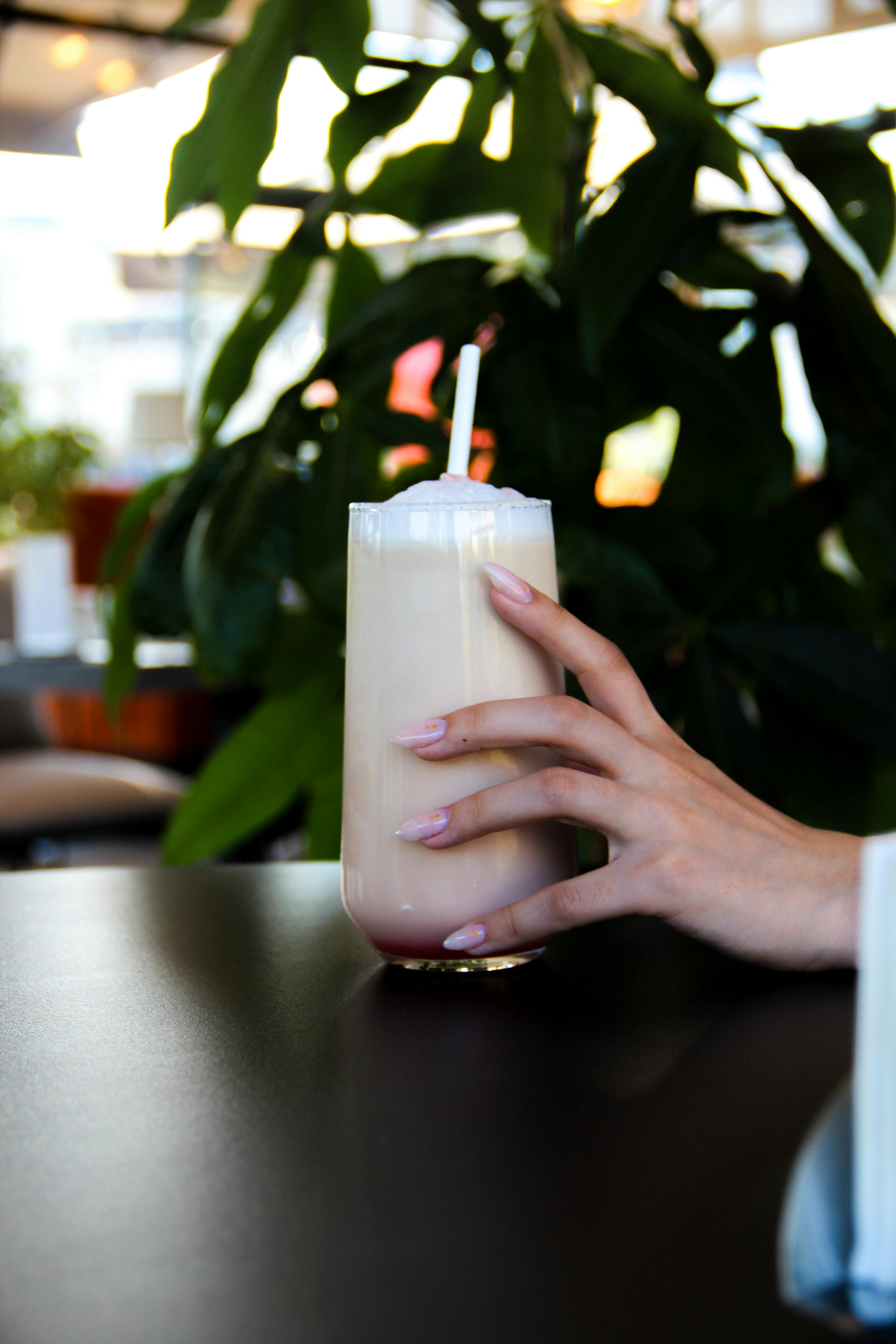 Free A woman's hand holding a glass of iced coffee with whipped cream and straw on a café table. Stock Photo
