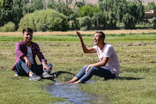 Smiling Men Sitting on Ground and Splashing Water