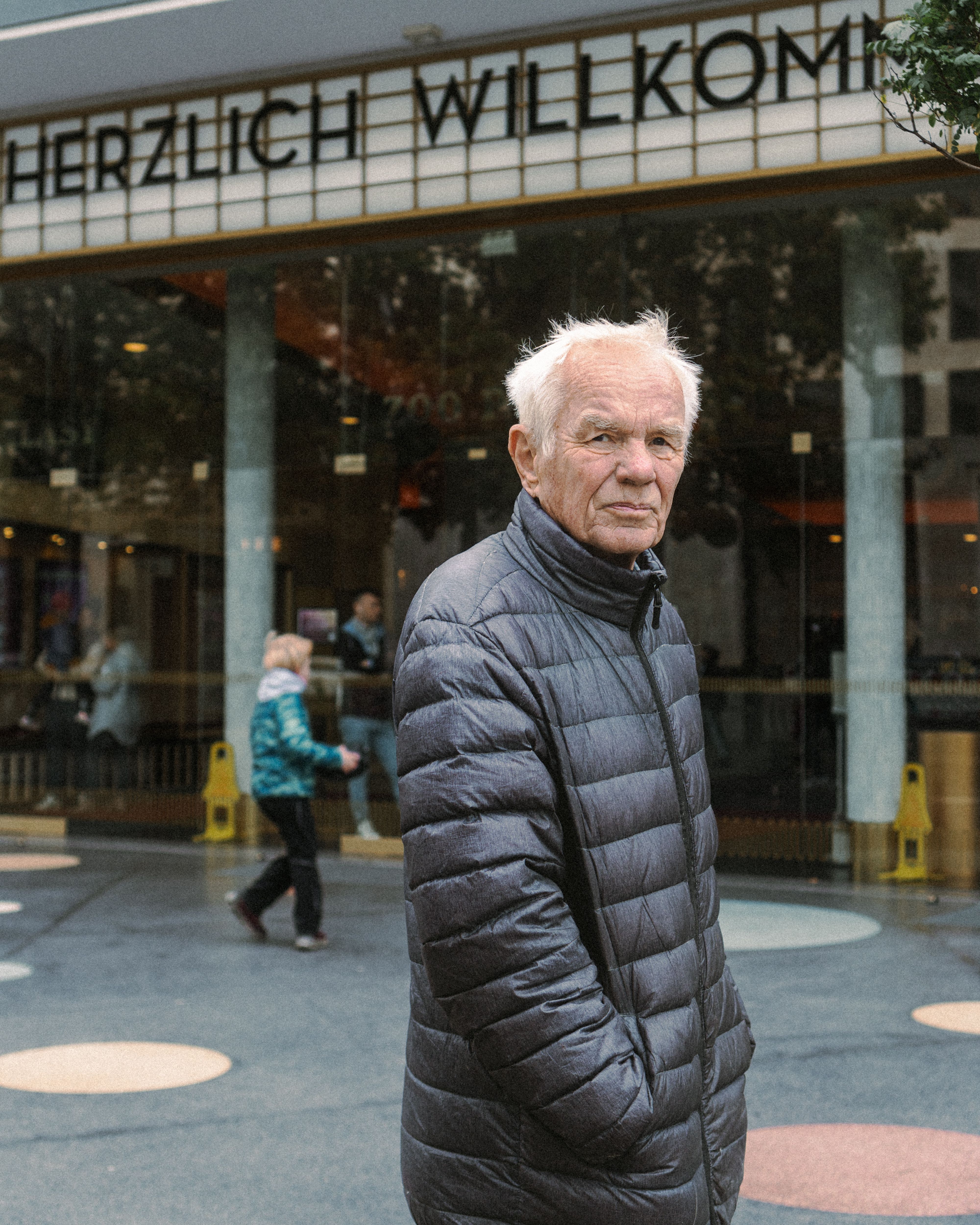 Senior man in a puffer jacket standing on a bustling Berlin street, capturing the essence of urban life.