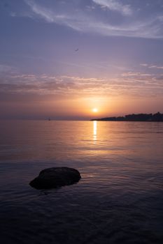 Beautiful sunrise over a tranquil seascape with a rock in the foreground. Perfect for peaceful themes.