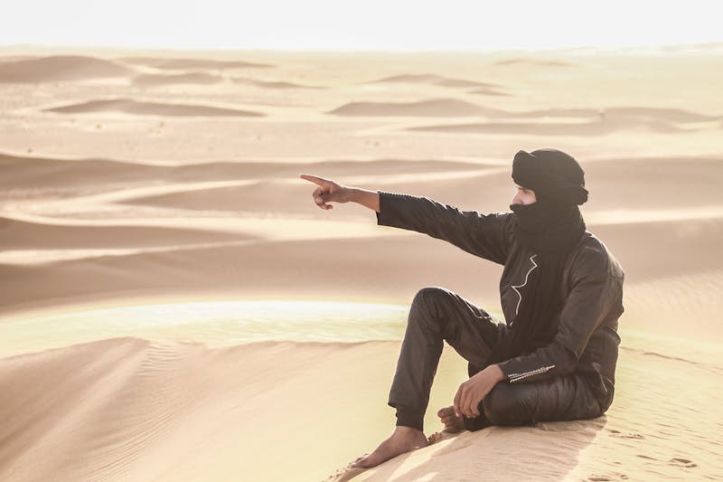 Homme en tenue traditionnelle indiquant les dunes du désert du Sahara