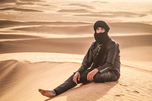 Man in Leather Jacket Sitting on Dune on Desert