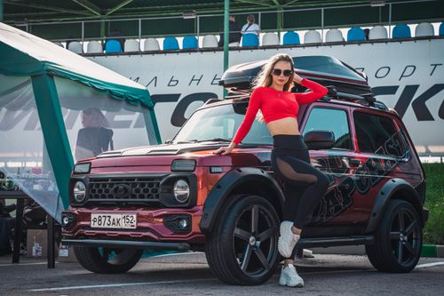 Free Young woman in a red crop top posing beside a stylish custom SUV at an outdoor motor show. Stock Photo