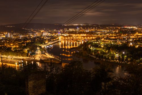 Free A scenic night view of Koblenz with illuminated riverbanks and buildings under a moonlit sky. Stock Photo