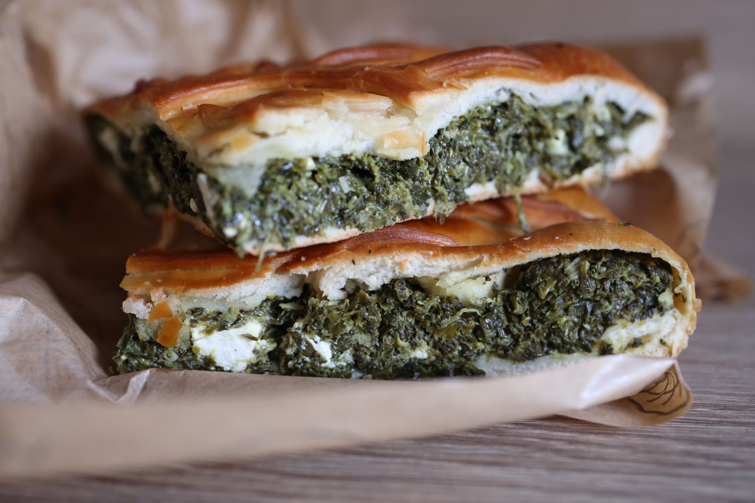 Thick slices of golden lattice pie filled with dark green spinach, white feta and herbs on parchment