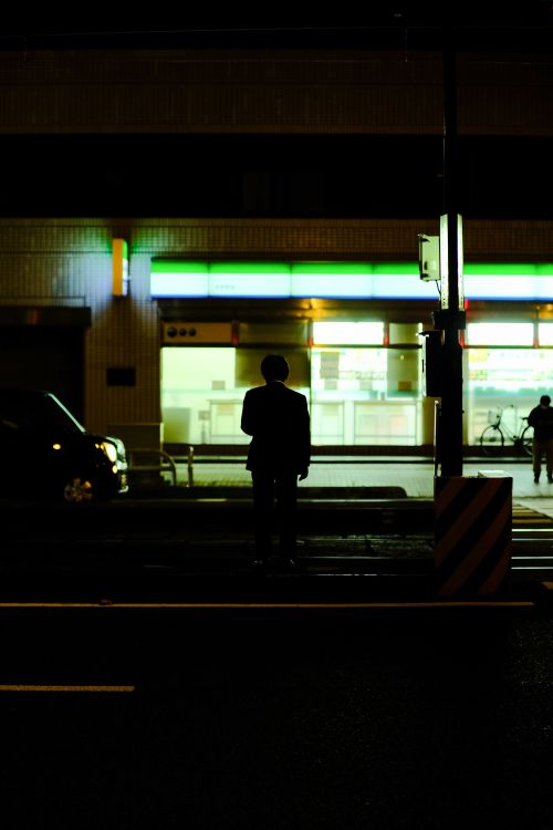 Free Silhouette of a man standing on the street at night with illuminated storefronts. Stock Photo