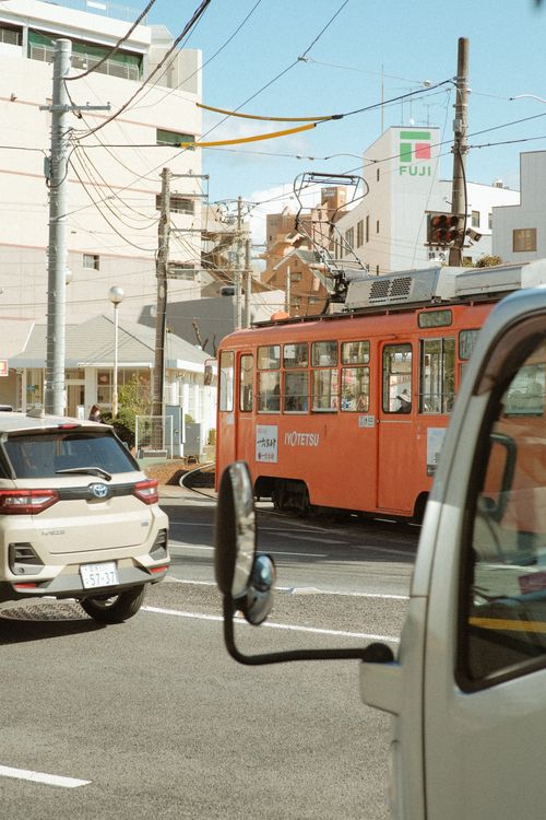 Free Vibrant city street in Matsuyama featuring an orange tram and surrounding traffic. Stock Photo