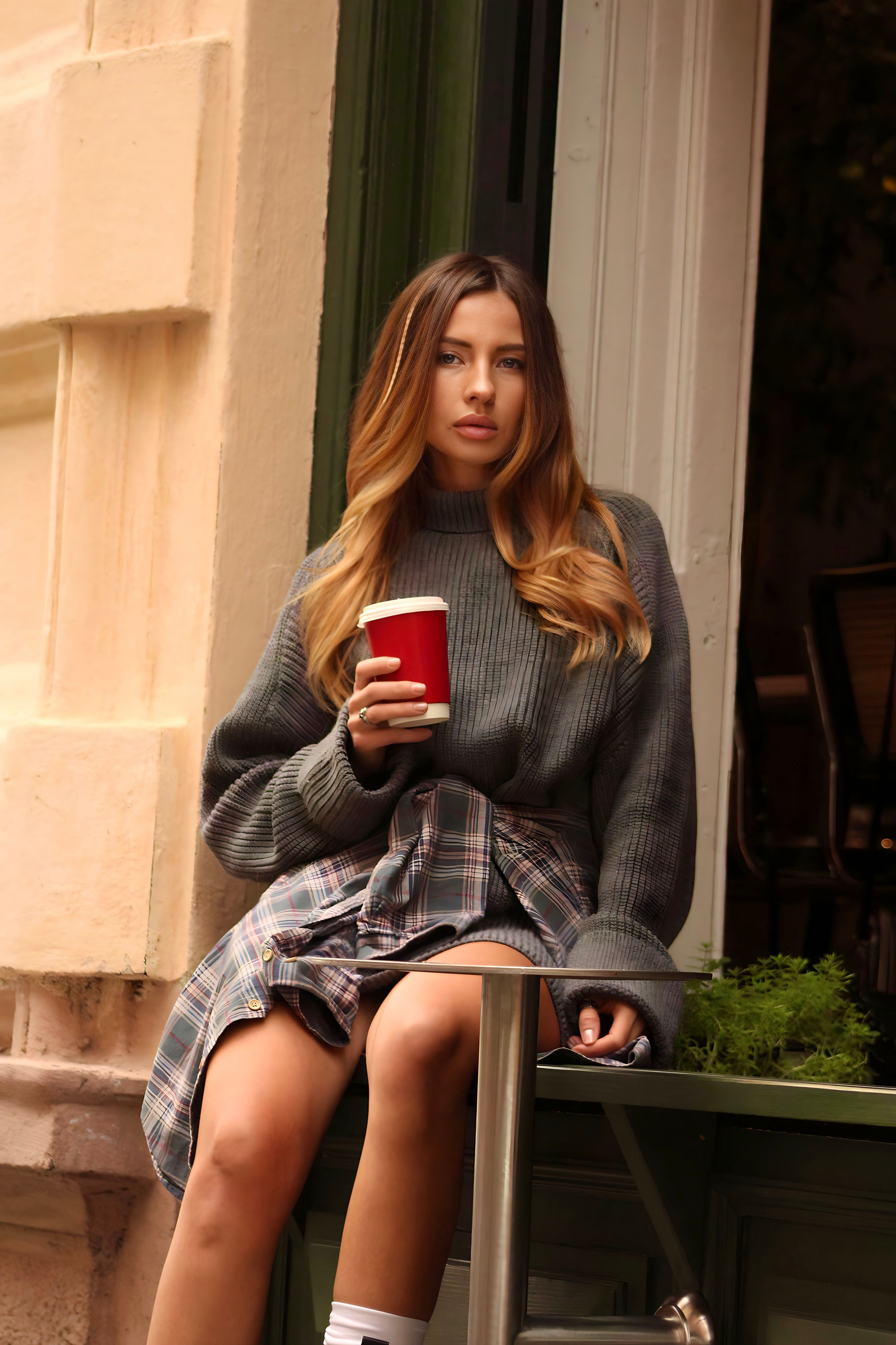 Young woman in trendy autumn outfit enjoys a coffee outside a café. Perfect lifestyle and fashion imagery.