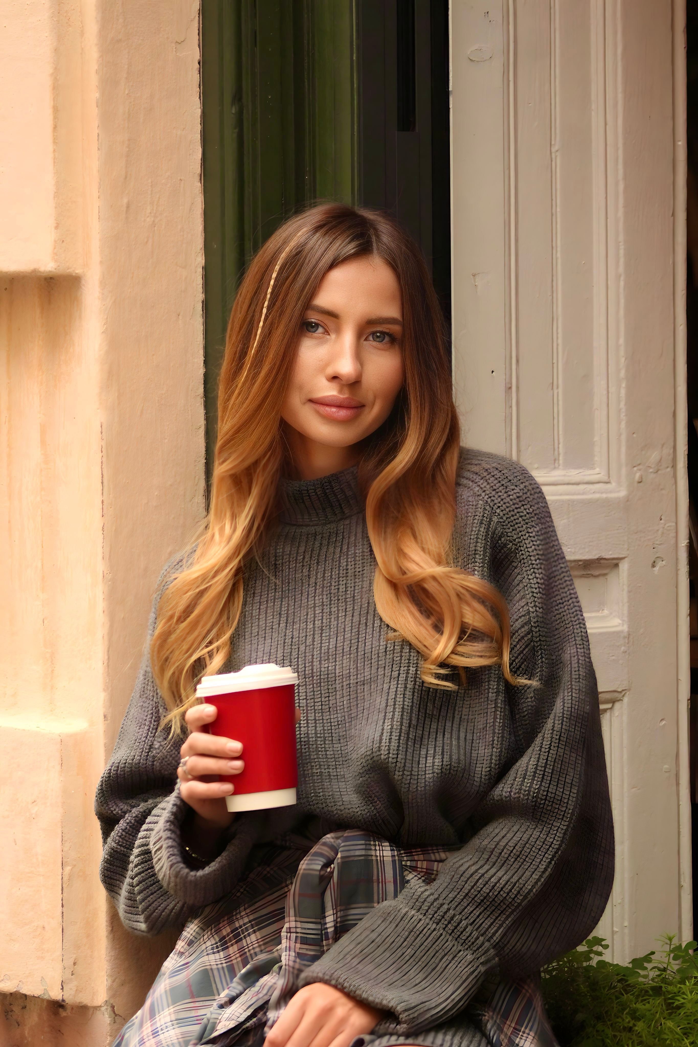 Young woman relaxing with a coffee outdoors in casual attire.