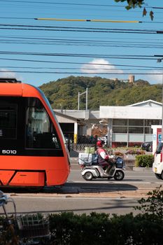 A bustling urban street scene featuring a vibrant orange tram and a commuter on a scooter.