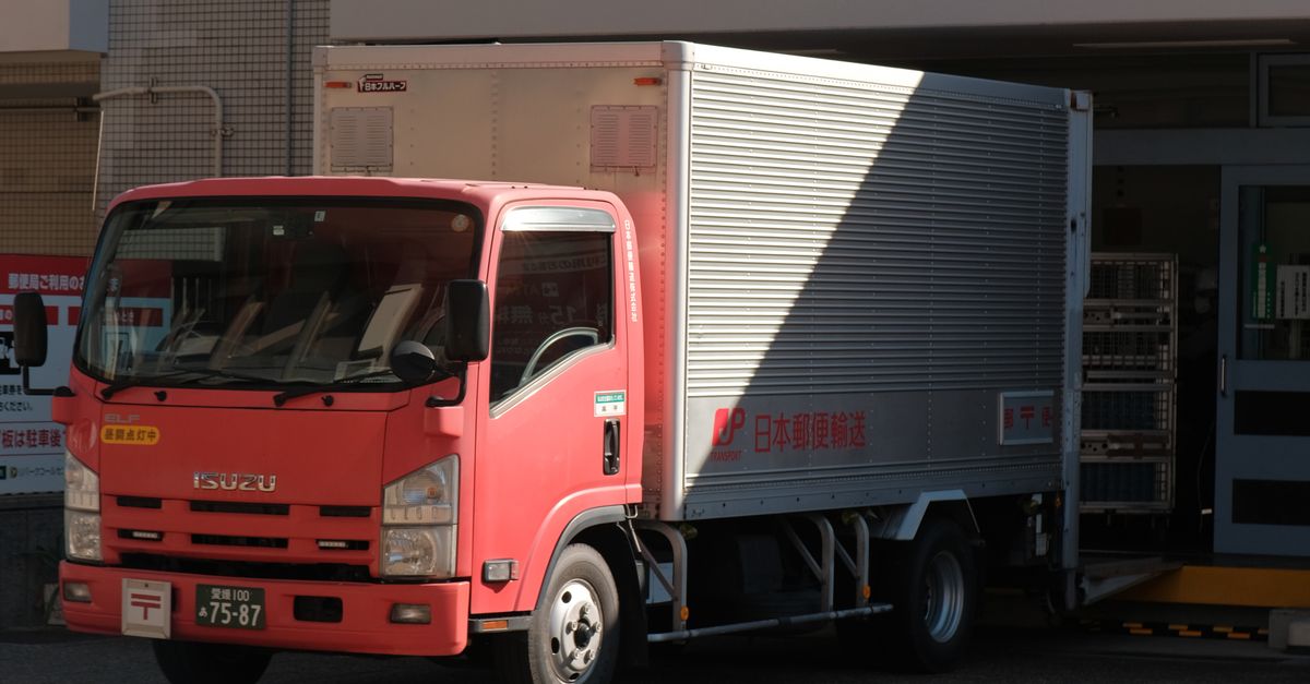 A red delivery truck unloading goods at a warehouse on a sunny day in the city.