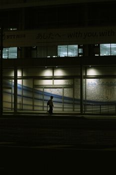 Silhouetted individual walking past illuminated urban building at night, creating a mysterious mood.