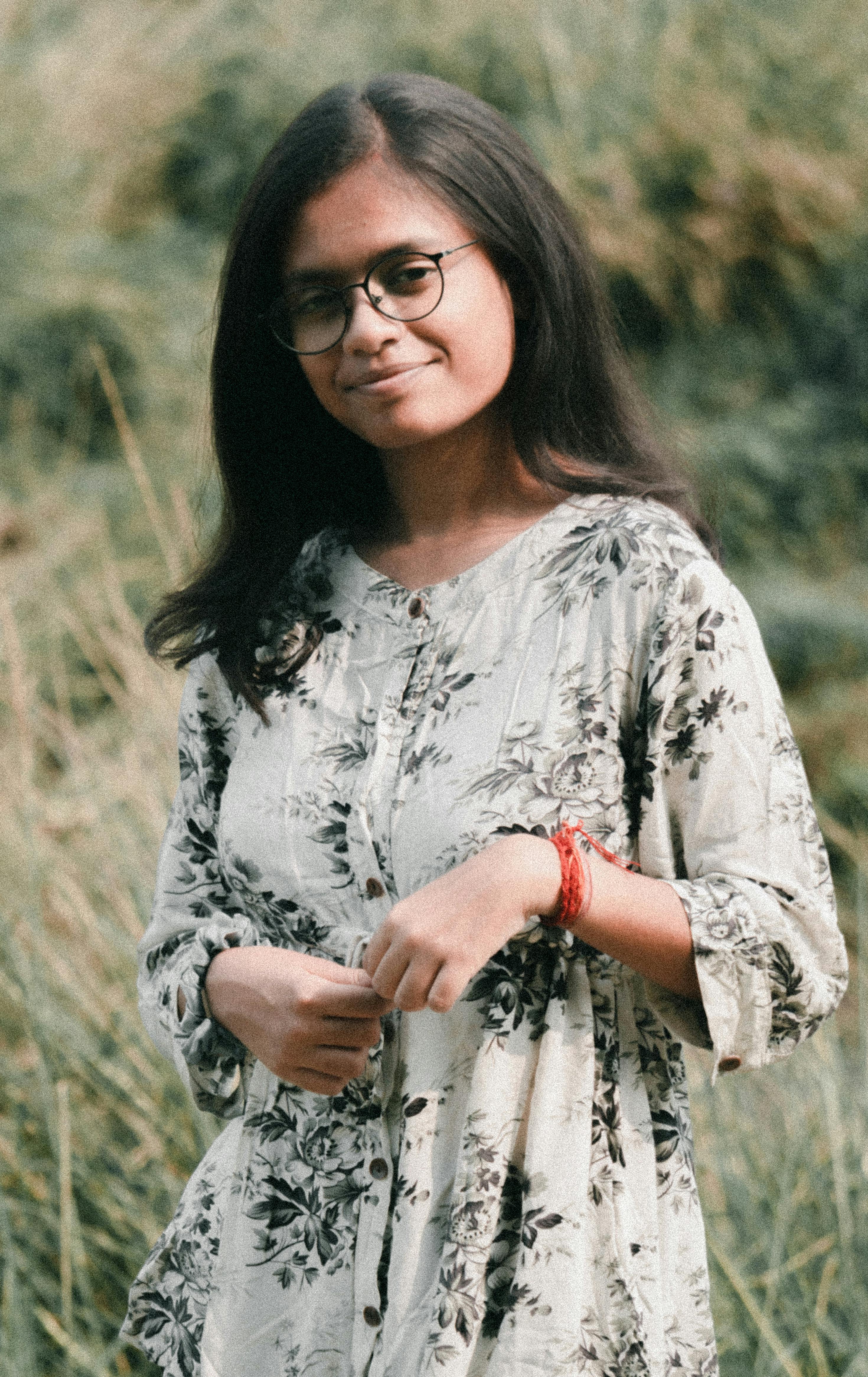 A serene portrait of a woman in glasses standing outdoors in a meadow.