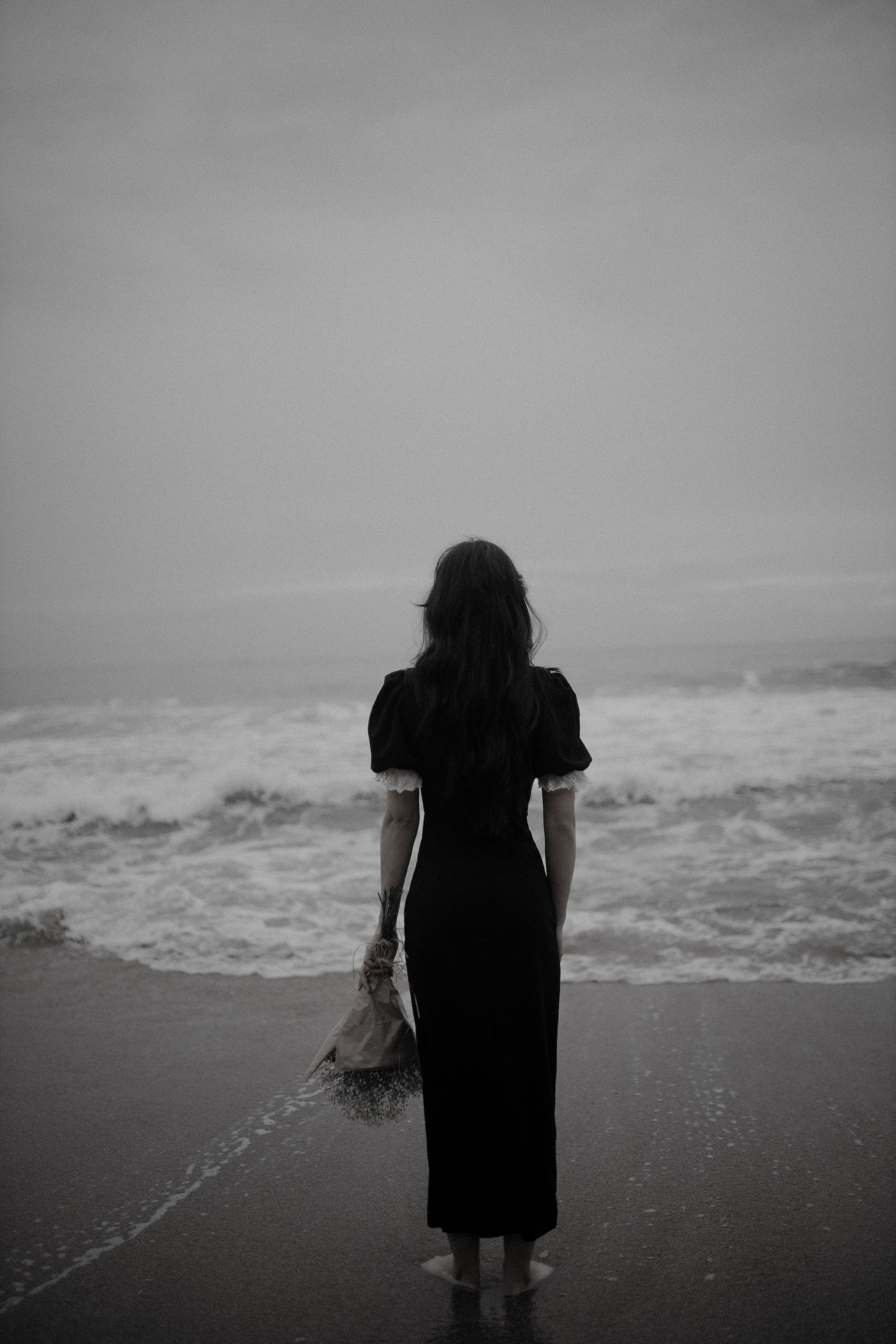 Black and White Photo of a Woman in Black Maxi Dress Standing on a Beach   Free Stock Photo