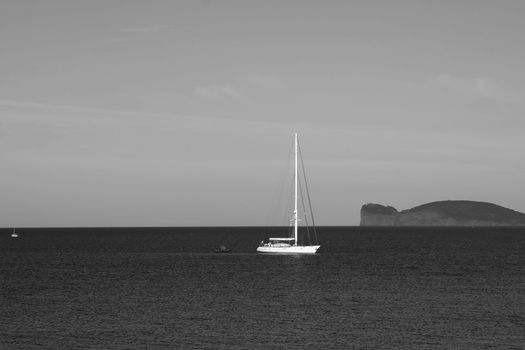 Monochrome image of a sailboat at sea near Alghero, Sardinia's coastline.