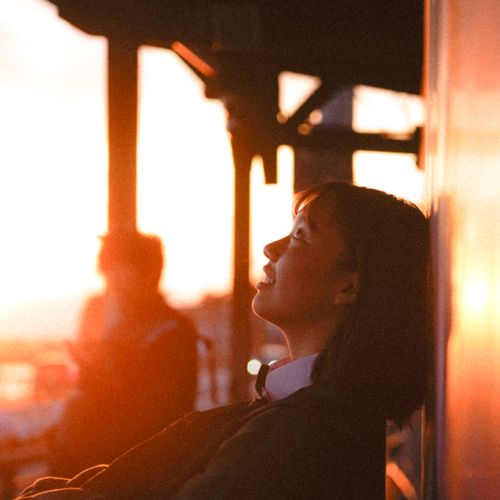 Free Asian woman with short hair smiles while leaning on a wall during sunset. Stock Photo