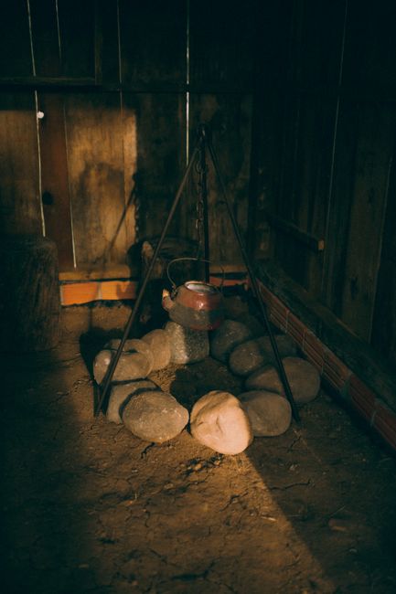 Photo by Alexander Mass on Pexels A cozy rustic scene featuring a kettle hung over stones in a wooden interior setting.