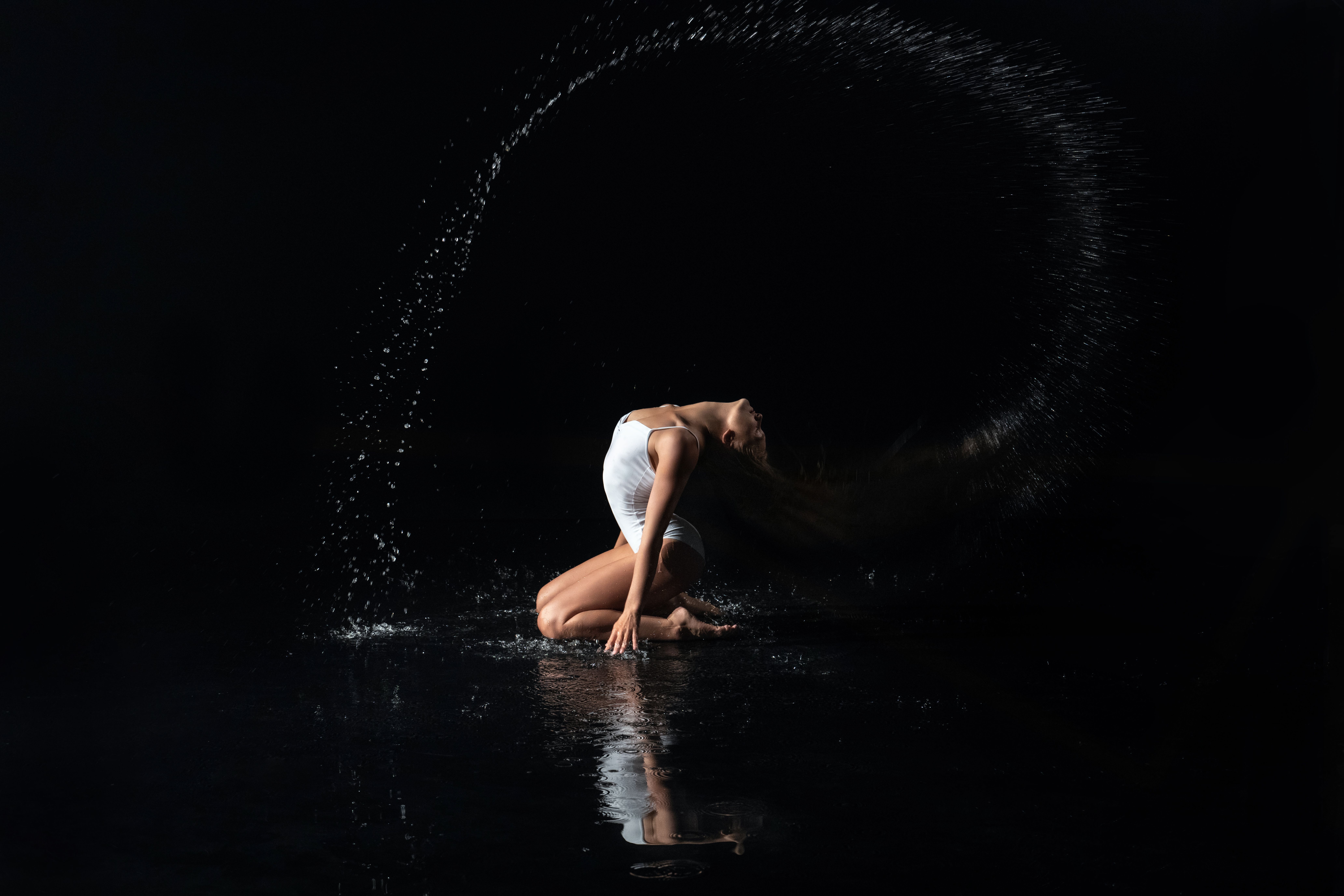 A woman gracefully dances with a water splash in a dramatic studio setting.