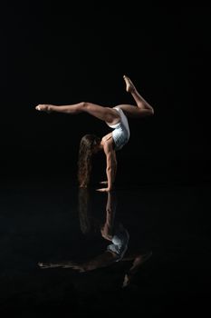 A ballet dancer performs a graceful handstand with a clear reflection on a black background.
