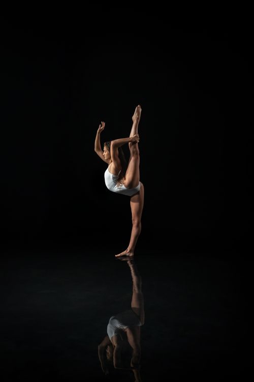 Free Ballet dancer in a graceful penché pose in a dark, reflective studio setting, showcasing flexibility. Stock Photo