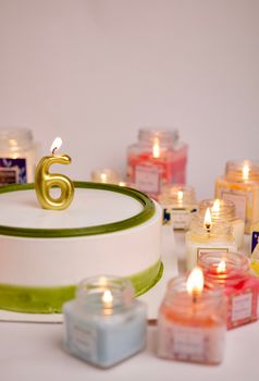 Vibrant birthday cake with number six candle surrounded by lit glass jar candles.