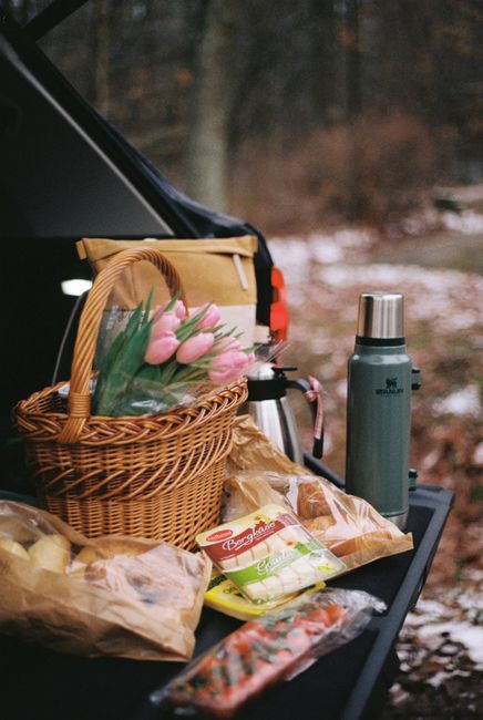 A cozy picnic setup with tulips, snacks, and a thermos in a winter forest setting.