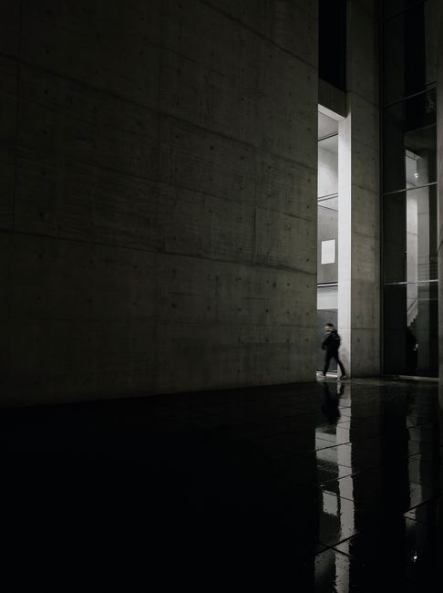 A lone figure walks through a modern concrete building at night, creating a dramatic urban scene.