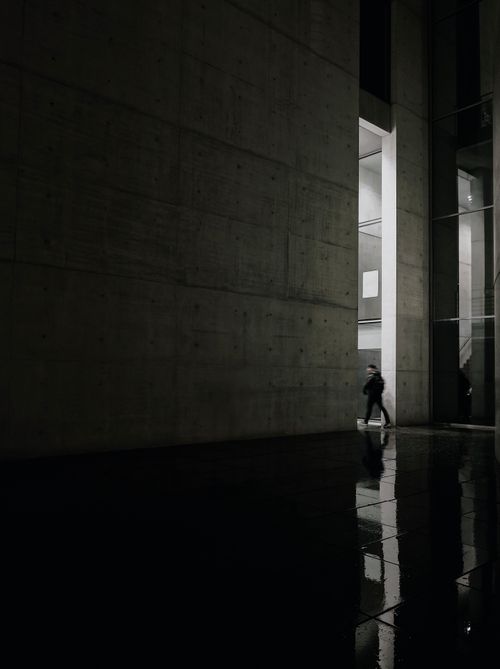 Free A lone figure walks through a modern concrete building at night, creating a dramatic urban scene. Stock Photo