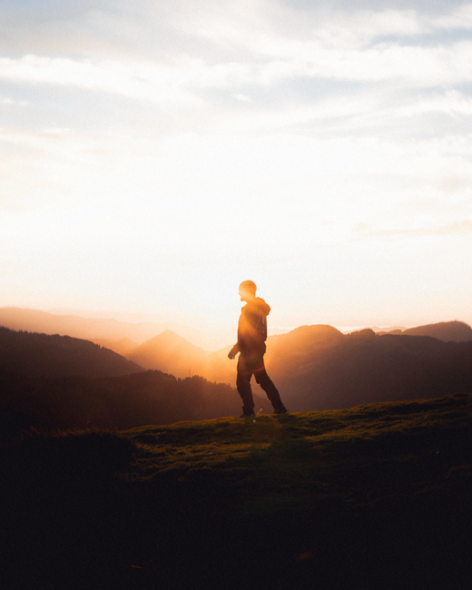 Silhouette of a man hiking on a hill during sunset, capturing serene rural landscape.