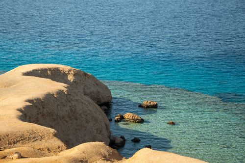 Free A serene coastal scene showcasing golden sand dunes next to crystal-clear blue waters. Stock Photo