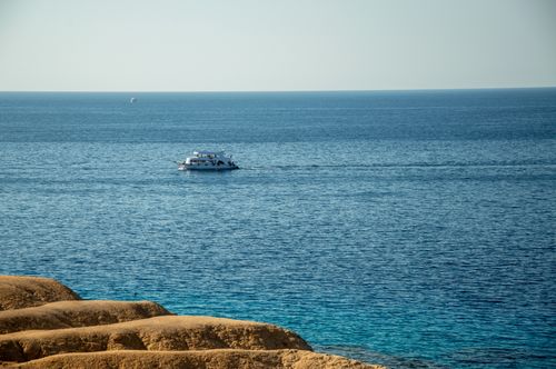 Free Calm sea with a boat cruising past golden rock formations under a clear sky. Stock Photo