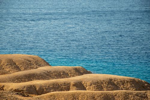 Free Golden rocky coastline meeting the tranquil blue ocean under a clear summer sky. Stock Photo