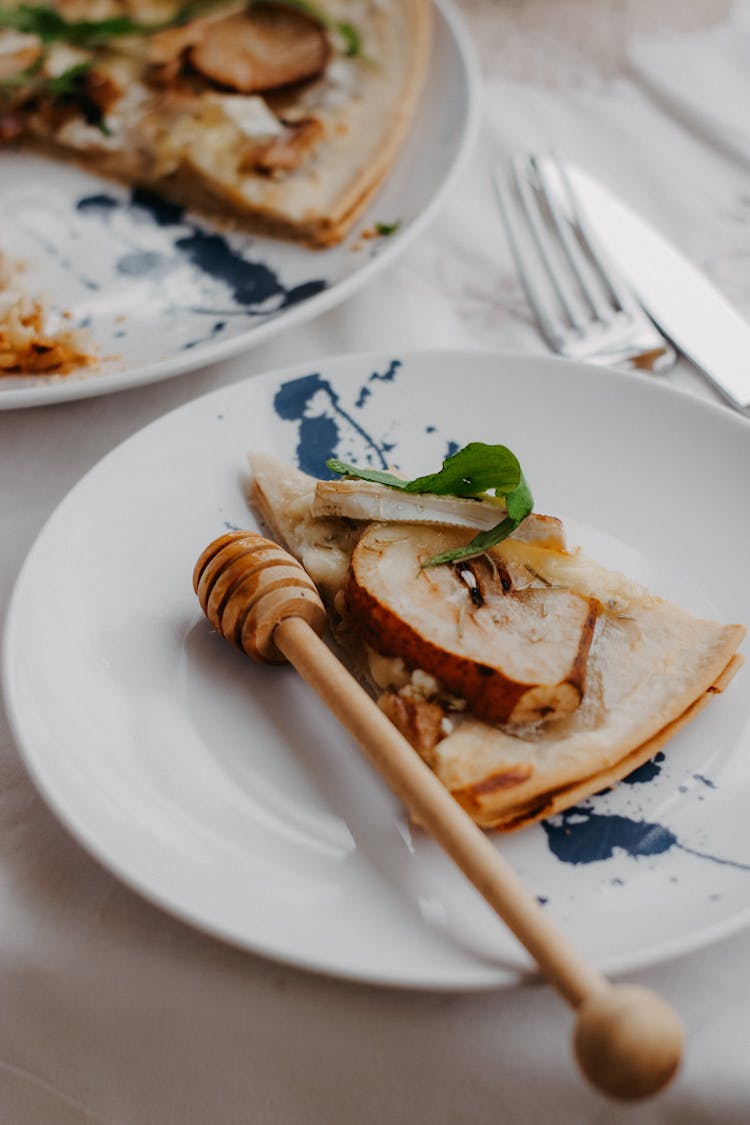 Slice Of Pear And Cheese Pizza And A Honey Dipper Lying On A White Plate