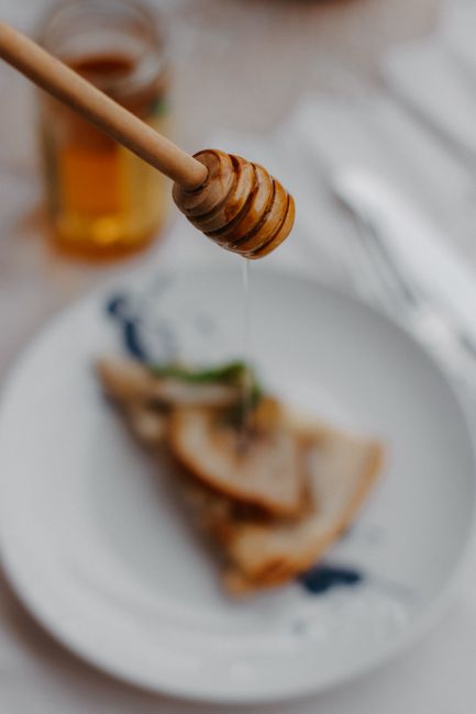 A glass jar of golden honey with a wooden honey dipper resting across the rim, next to a smaller jar of pale, grainy crystallized honey for comparison.