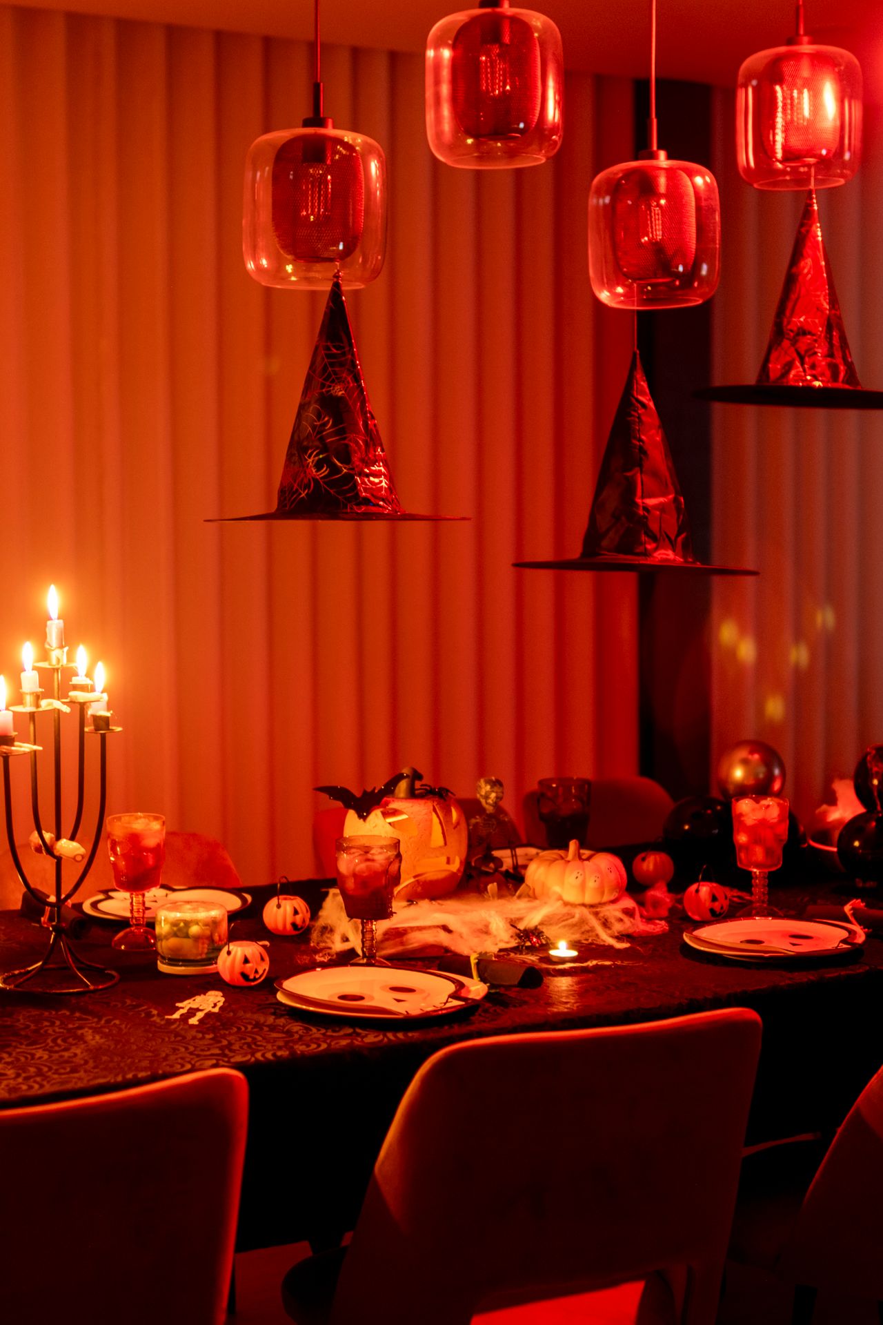 Dramatic Halloween dinner table with floating witch hats, red lighting, and pumpkin decor