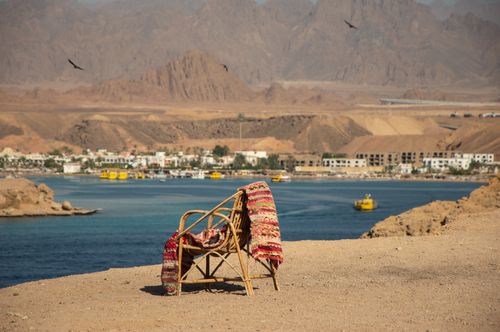 Free A chair draped with a colorful blanket overlooks a serene desert coastline. Stock Photo