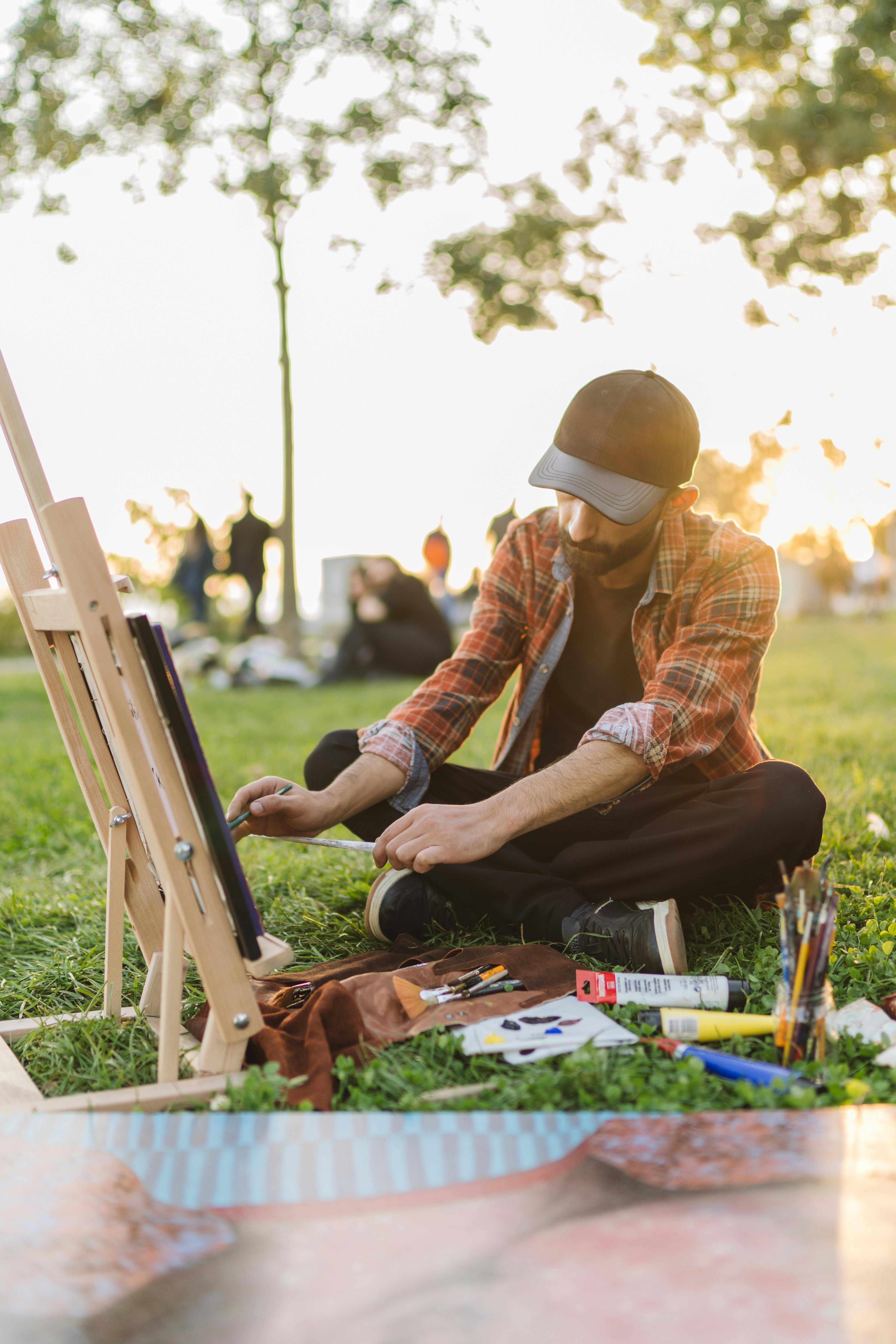 Man in Red Flannel Shirt and Black Baseball Cap Painting on an Easel