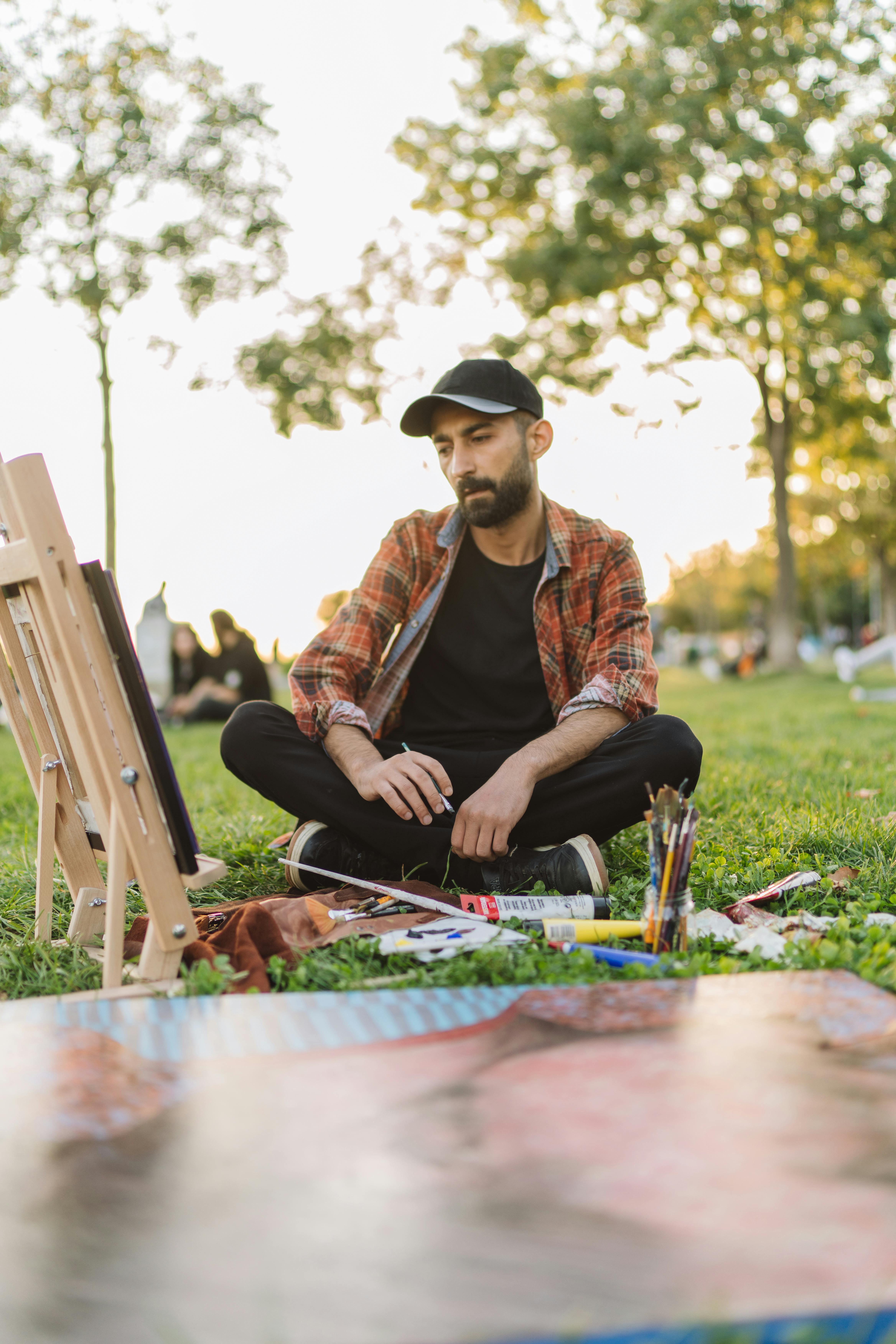 Man in Red Flannel Shirt and Black Baseball Cap Sitting on a Lawn by an