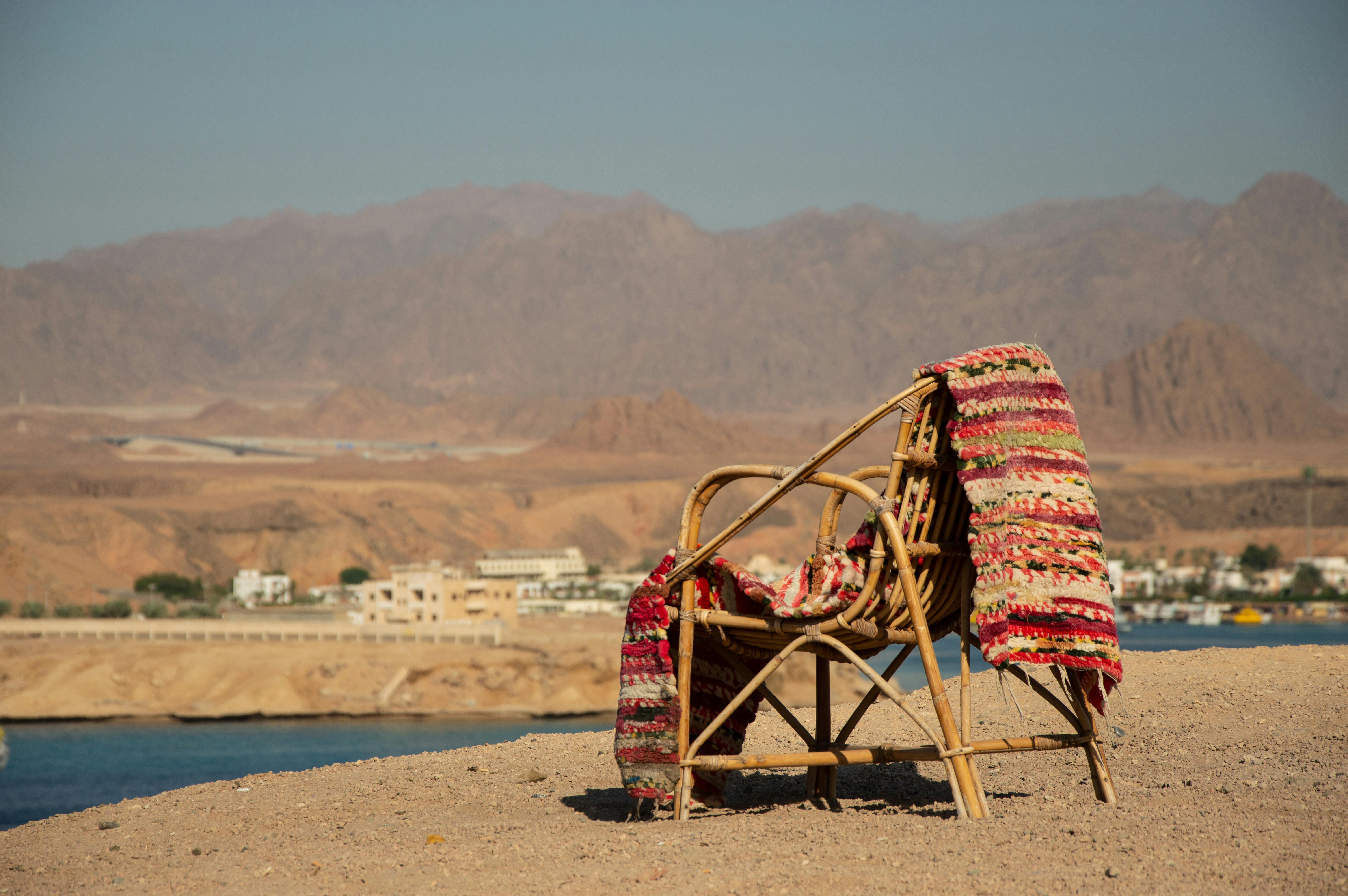 A cozy rattan chair with a colorful rug on a sandy beach, ideal for a serene vacation.