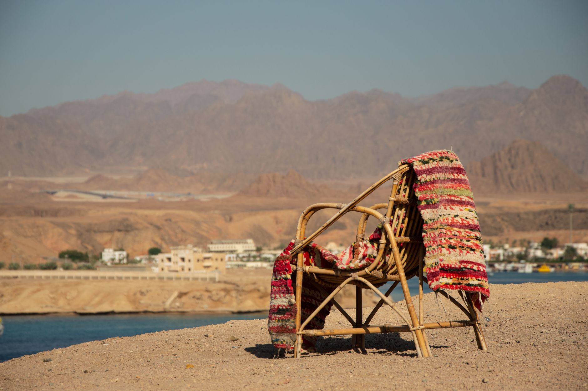 A cozy rattan chair with a colorful rug on a sandy beach, ideal for a serene vacation.