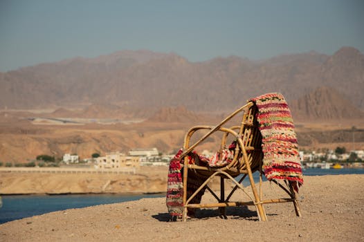 A cozy rattan chair with a colorful rug on a sandy beach, ideal for a serene vacation.