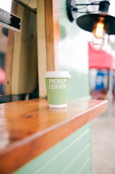 A green coffee cup labeled 'Pickup Coffee' on a wooden counter outdoors, daytime.